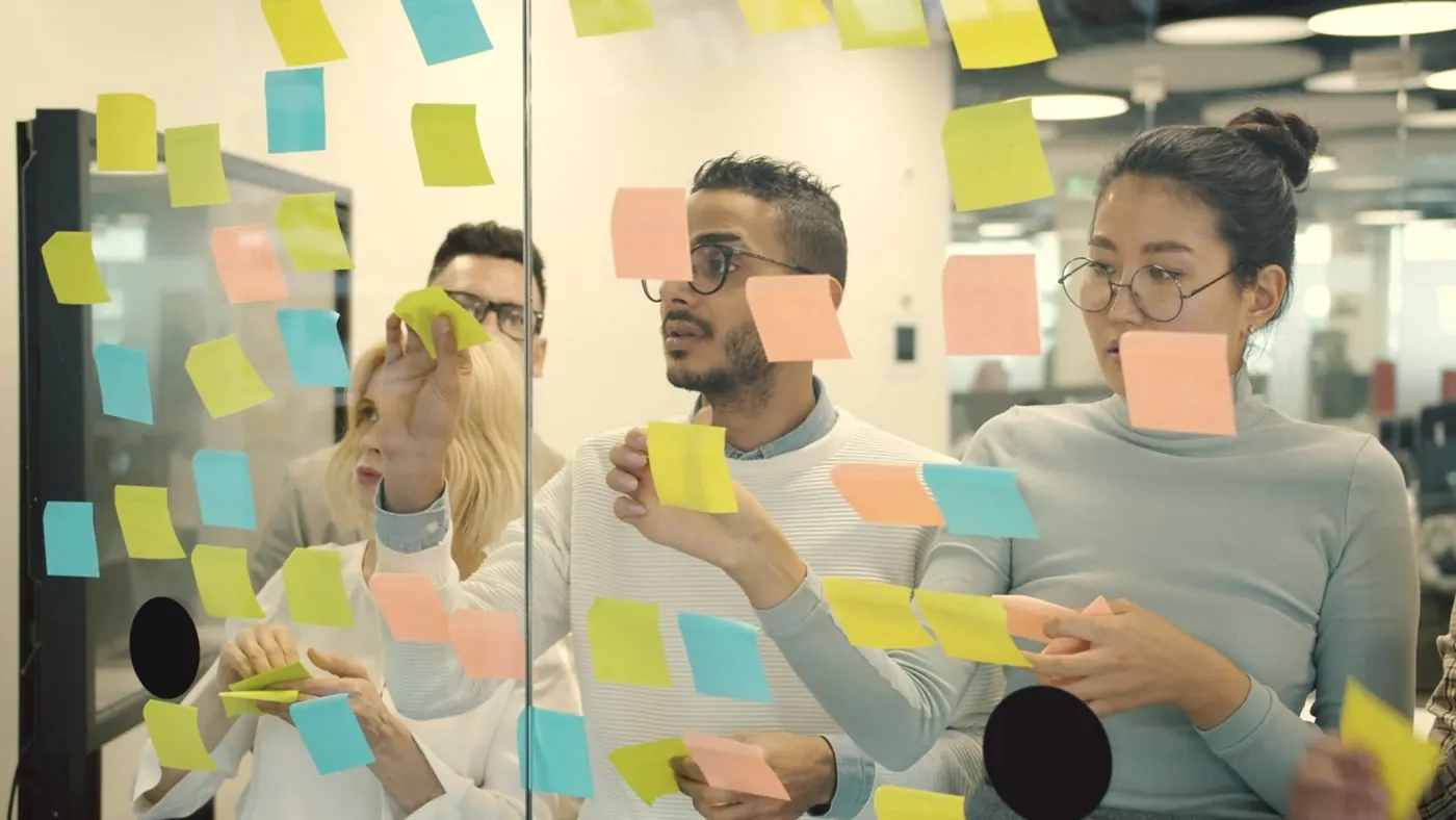 Une équipe colle des post-it sur une paroi vitrée pendant un atelier