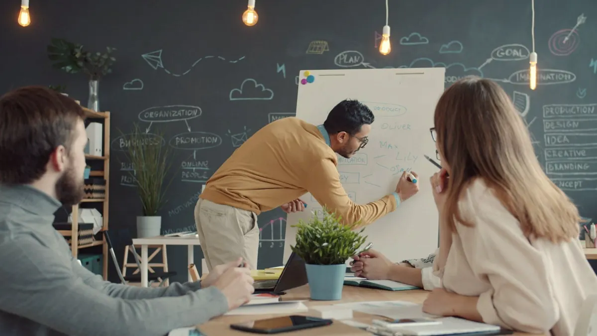 Un manager note au tableau pendant qu'une collègue prend des notes